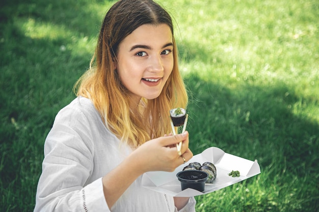 Una chica hermosa come sushi sentada en el césped del parque