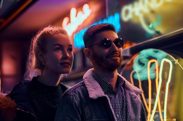 Una chica hermosa y un hombre guapo parados en la noche en la calle. Letreros iluminados, neón, luces.