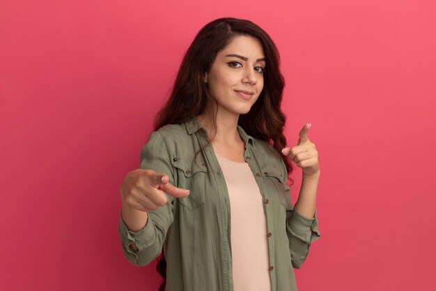 Chica hermosa joven complacida con camiseta verde oliva que le muestra gesto aislado en la pared rosa