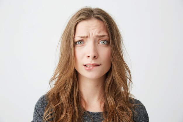 Chica hermosa joven nerviosa frunciendo el ceño mordiendo el labio.