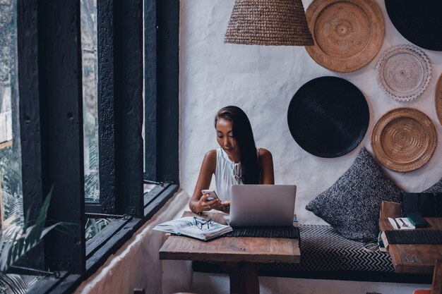 Chica hermosa joven utiliza una computadora portátil en el café, navegar por internet