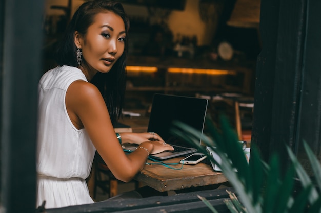 Chica hermosa joven utiliza una computadora portátil en el café, navegar por internet