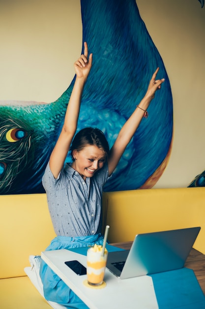 Chica hermosa joven utiliza una computadora portátil en el café, navegar por internet