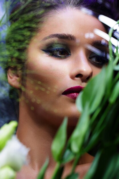 Chica hermosa de moda con maquillaje brillante entre flores.