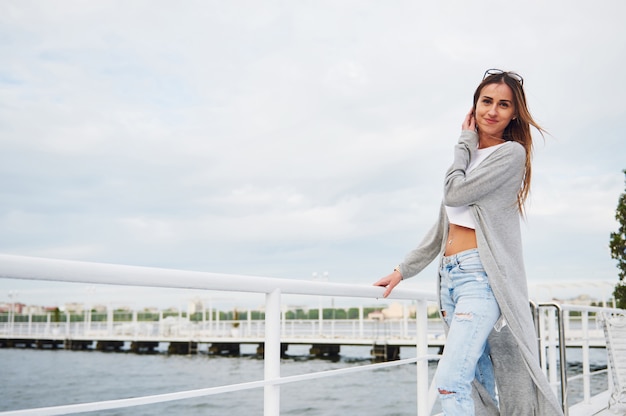 Chica hermosa sonrisa de pie en un muelle cerca del agua.