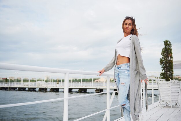 Chica hermosa sonrisa de pie en un muelle cerca del agua.