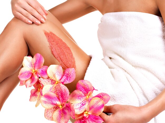 La chica con un hermoso cuerpo con flor con un exfoliante en la pierna sobre un fondo blanco.