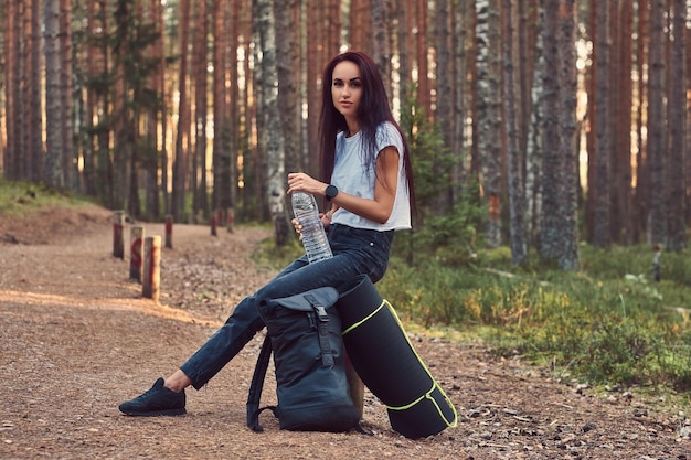 Chica hipster turista sostiene una botella de agua, se detuvo a descansar en el hermoso bosque de otoño.