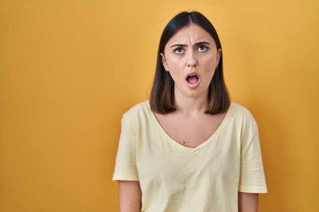 Chica hispana con camiseta informal sobre fondo amarillo enojada y enojada gritando frustrada y furiosa gritando con ira, rabia y concepto agresivo