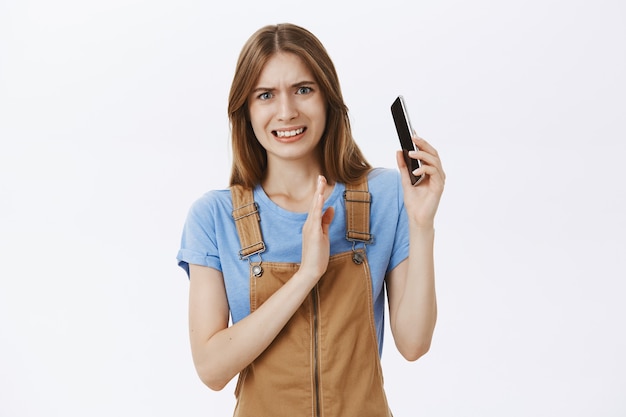 Chica incómoda y disgustada se inclina lejos del teléfono móvil cuando alguien le grita durante una conversación