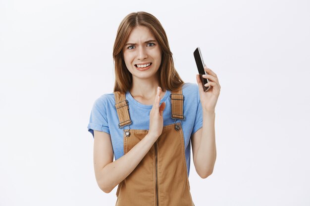 Chica incómoda y disgustada se inclina lejos del teléfono móvil cuando alguien le grita durante una conversación