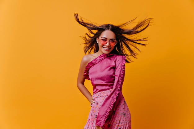 Chica increíblemente hermosa con una sonrisa radiante con confianza y audacia, posando en una blusa de moda para el retrato en la pared aislada