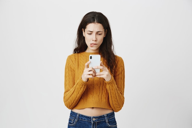 Chica indecisa recibe un mensaje frustrante, mirando indeciso al teléfono móvil