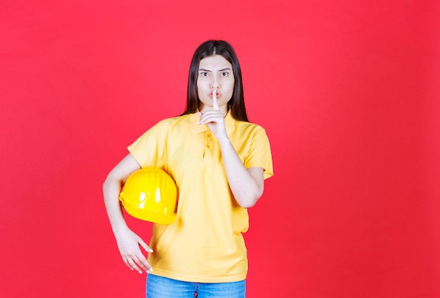 Chica ingeniera en código de vestimenta amarillo sosteniendo un casco de seguridad amarillo y pidiendo firma.