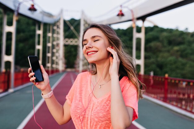 Chica inspirada escuchando música con los ojos cerrados después del entrenamiento al aire libre Mujer bonita rubia disfrutando del entrenamiento con su canción favorita