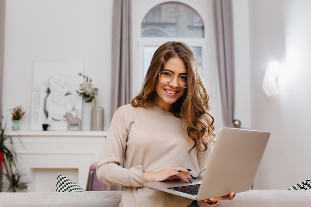 Foto gratuita chica inteligente complacida con elegante peinado rizado disfrutando de una sesión de fotos con una computadora portátil