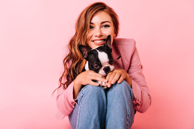 Chica interesada con peinado ondulado pasar tiempo libre con perro. retrato de mujer joven posando con bulldog francés.