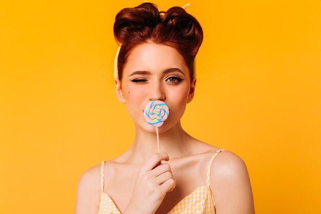 Chica de jengibre elegante lamiendo piruleta. Vista frontal de la mujer entusiasta con caramelos.