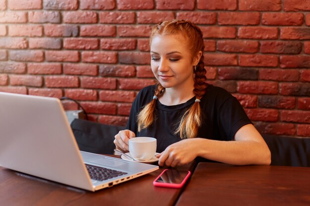 Chica de jengibre usa laptop en café