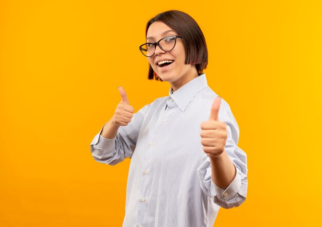 Chica joven alegre del centro de llamadas con gafas mostrando los pulgares para arriba aislado en naranja