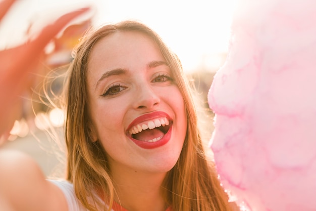 Chica joven con algodón de azúcar en el parque de atracciones