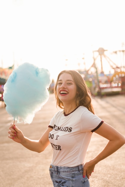 Chica joven con algodón de azúcar en el parque de atracciones