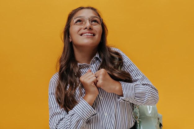 Chica joven en anteojos mira soñadoramente Feliz adolescente bronceado en camisa a rayas sonríe y posa sobre fondo naranja