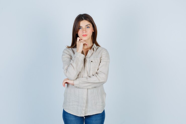 Foto gratuito chica joven apoyando la barbilla en la mano con camisa beige, jeans y mirando serio, vista frontal.
