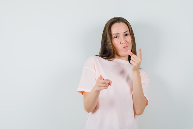 Chica joven apuntando en camiseta rosa y mirando confiado. vista frontal.