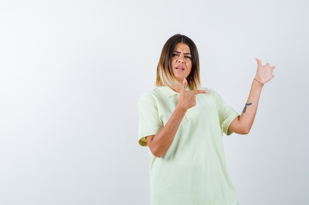 Chica joven apuntando a la derecha en camiseta y mirando seria. vista frontal.