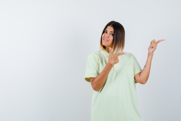 Foto gratuita chica joven apuntando a la derecha con los dedos índices en camiseta y mirando alegre. vista frontal.