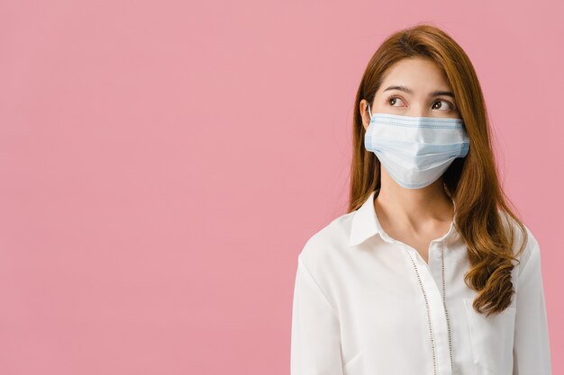 Chica joven de Asia con mascarilla médica vestida con ropa casual y mirando el espacio en blanco aislado sobre fondo rosa.