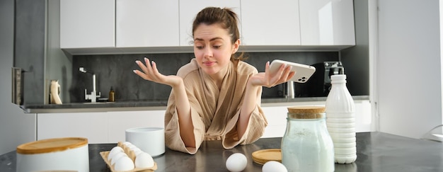 Foto gratuita chica joven atractiva y alegre horneando en la cocina haciendo masa sosteniendo un libro de recetas teniendo ideas