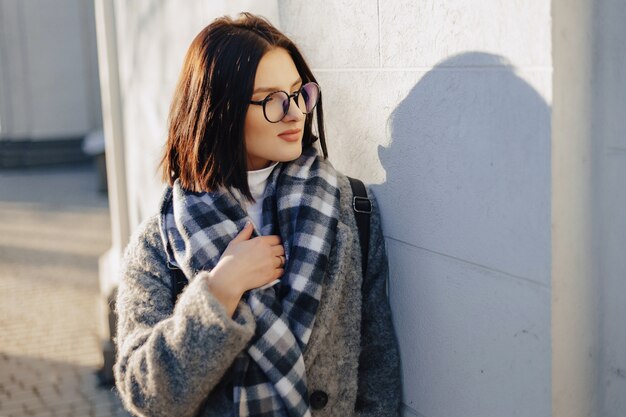 Chica joven atractiva con gafas en un abrigo caminando en un día soleado