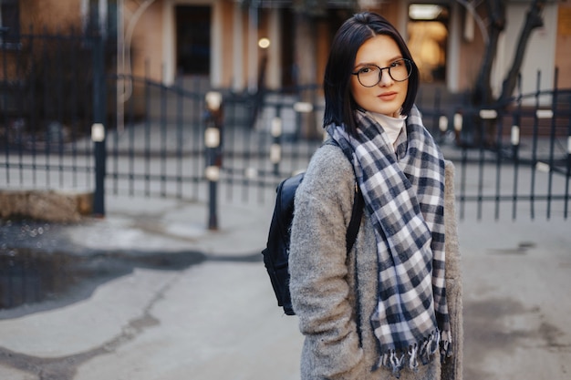 Chica joven atractiva con gafas en un abrigo caminando en un día soleado