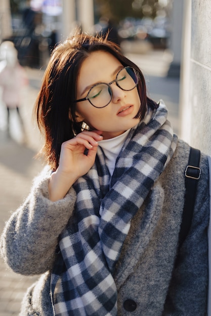 Chica joven atractiva con gafas en un abrigo caminando en un día soleado