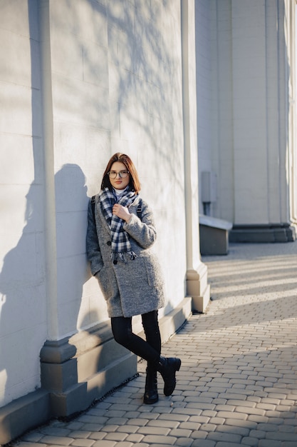 Chica joven atractiva con gafas en un abrigo caminando en un día soleado