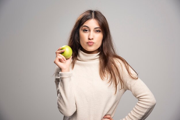 Una chica joven y atractiva con una manzana verde sobre una pared gris.