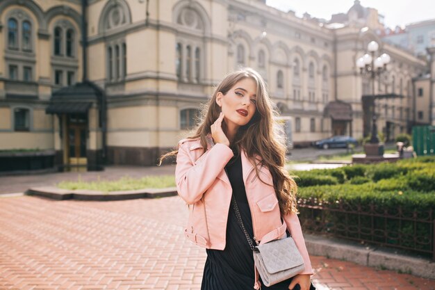 Chica joven atractiva con pelo largo y rizado y labios rojos posando en la ciudad.