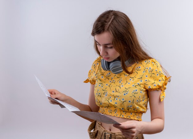 Chica joven con auriculares en el cuello y sosteniendo el mapa y mirándolo en la pared blanca aislada