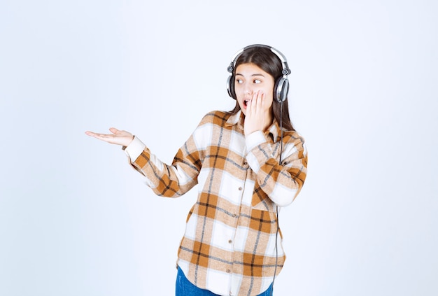 chica joven en auriculares mostrando algo en la pared blanca.