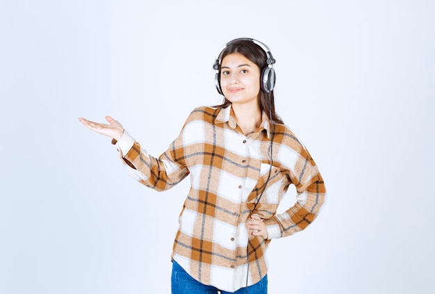 chica joven en auriculares de pie en la pared blanca.