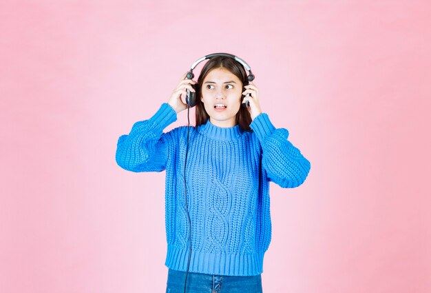 chica joven en auriculares de pie en rosa.