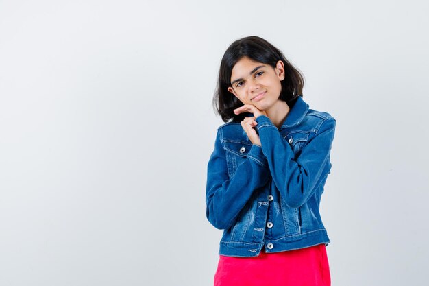 Chica joven con la barbilla apoyada en las manos en camiseta roja y chaqueta de jean y luciendo lindo