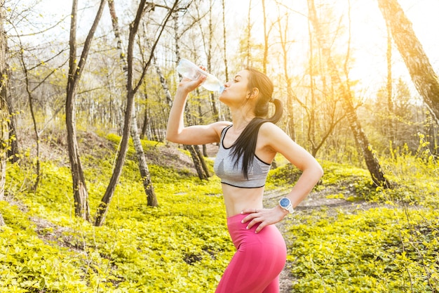 Chica joven bebiendo agua en la naturaleza