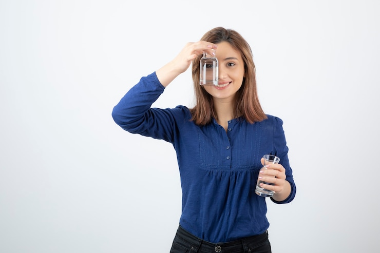 Foto gratuito chica joven en blusa azul mostrando un vaso de agua.