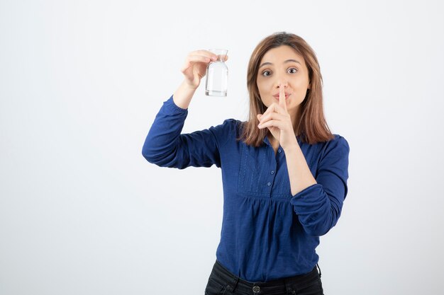 Chica joven en blusa azul sosteniendo agua y dando señal de silencio.