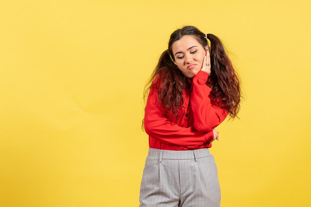 Chica joven en blusa roja posando con cara aburrida en amarillo