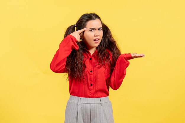 Chica joven en blusa roja posando con cara confundida en amarillo