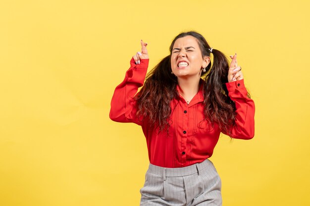 Chica joven en blusa roja posando cruzando los dedos sobre amarillo